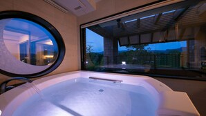 A modern bathroom with a large bathtub, a round mirror, and a view of a building and trees through a large window.