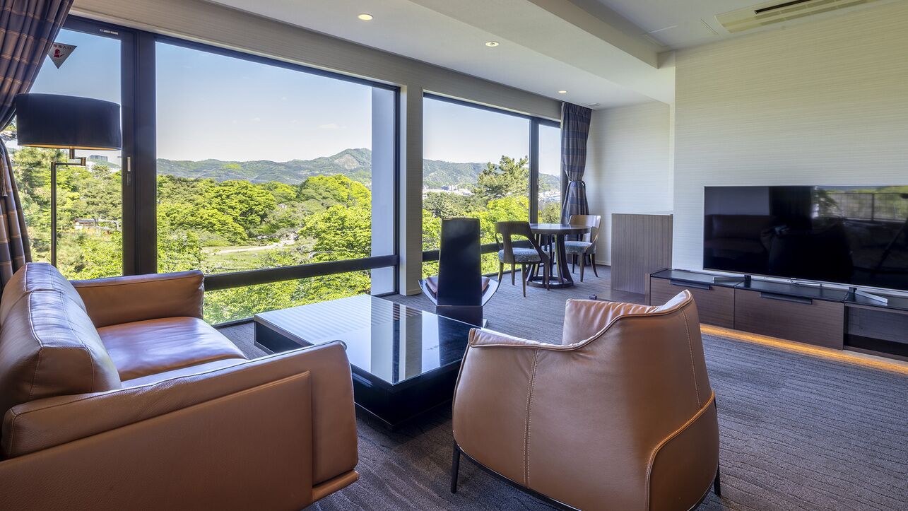 Ein modernes Hotelzimmer mit großem Fenster, Flachbildfernseher, Ledersofas und Essbereich.