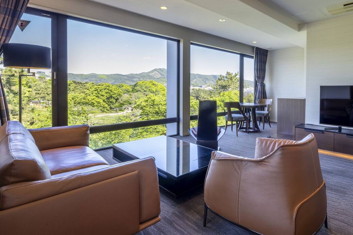 Une chambre d’hôtel moderne dotée d’une grande fenêtre, d’un téléviseur à écran plat, de canapés en cuir et d’un coin repas.