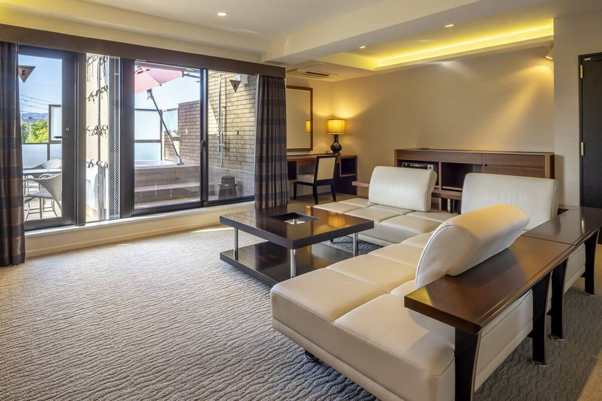 Une chambre d'hôtel équipée d'un canapé, d'une table basse, d'un téléviseur, d'un bureau et d'une grande porte-fenêtre coulissante donnant sur un espace extérieur.
