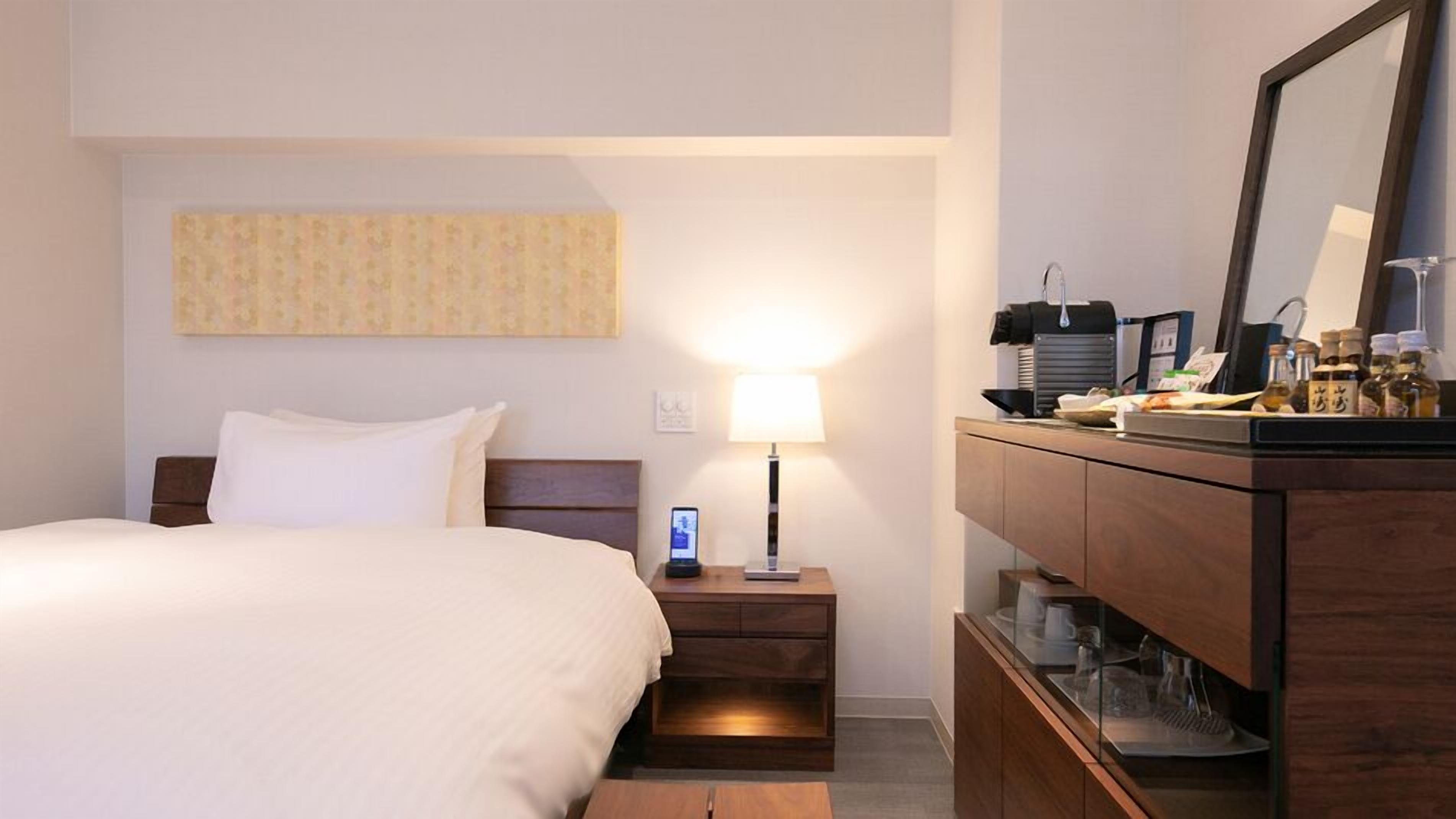 Ein Hotelzimmer mit Bett, Nachttisch, Lampe, Spiegel und einer Minibar.