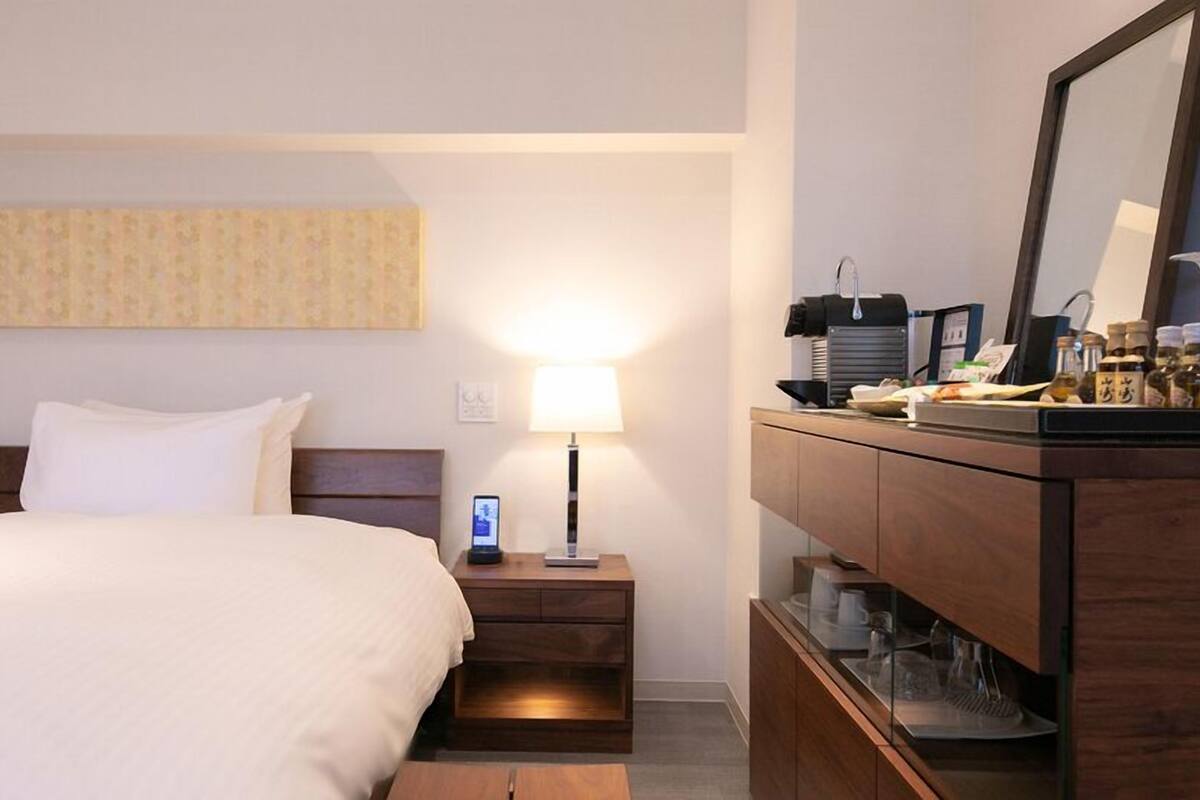 Une chambre d’hôtel équipée d’un lit, d’une table de chevet, d’une lampe, d’un miroir et d’un mini-bar.