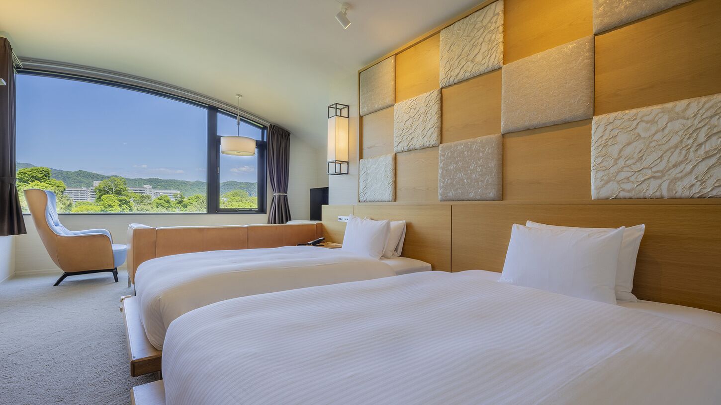 Ein Hotelzimmer mit zwei Betten, einem großen Fenster, einem Sessel und einer Wandverkleidung.
