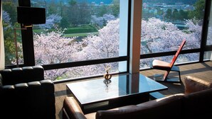 A modern interior with a sofa, a coffee table, and a chair, with a large window offering a view of cherry blossoms.