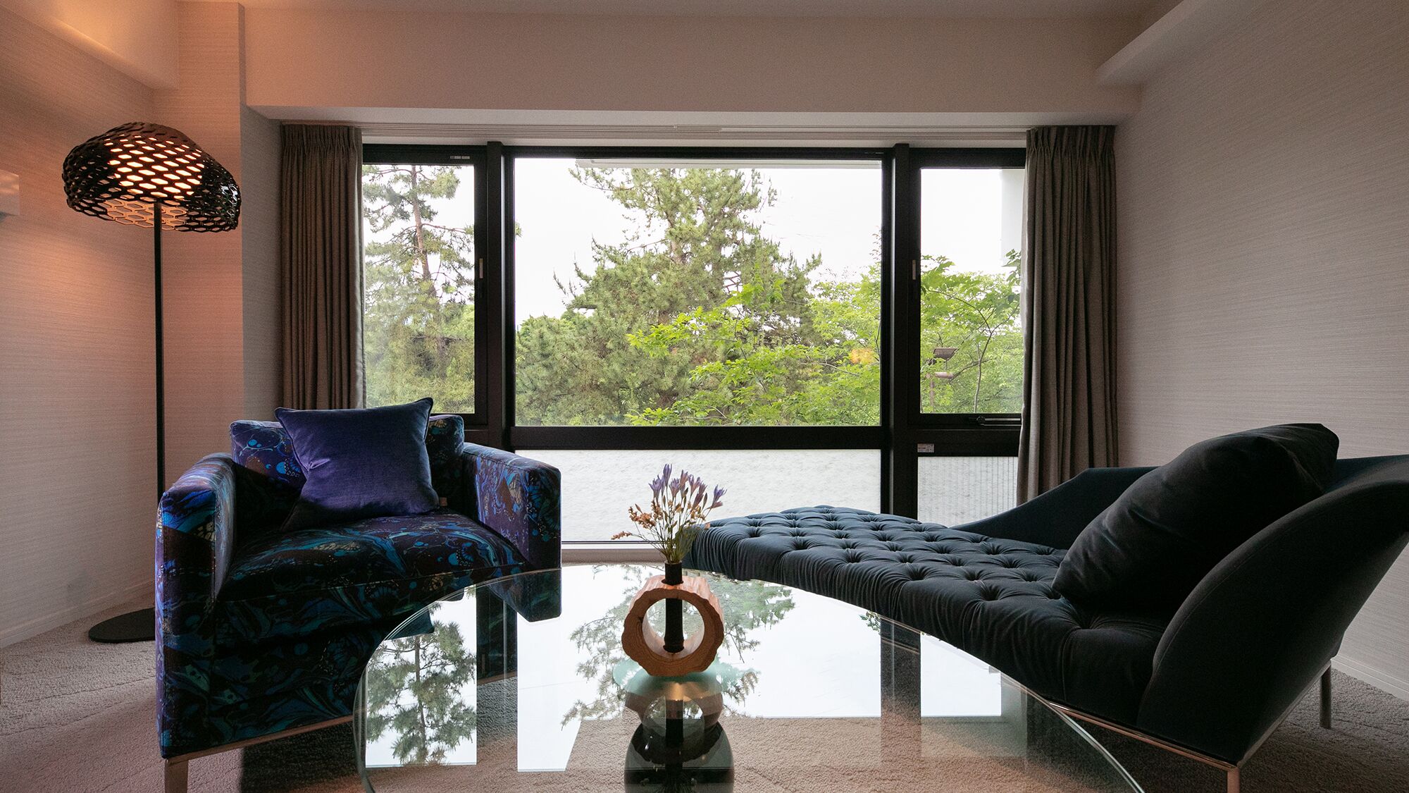 Ein modernes Wohnzimmer mit einem Glastisch, zwei Sofas und einem großen Fenster mit Vorhängen.