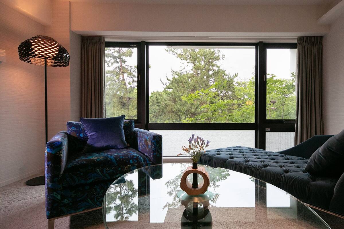 Un salon moderne avec une table basse en verre, deux canapés et une grande fenêtre avec des rideaux.