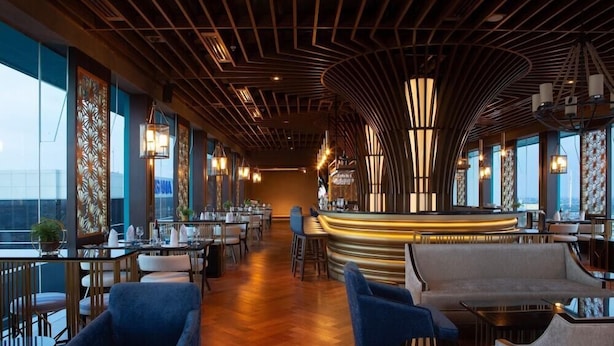 Un restaurant modern amb una barra corbada, sostre de fusta i grans finestres.