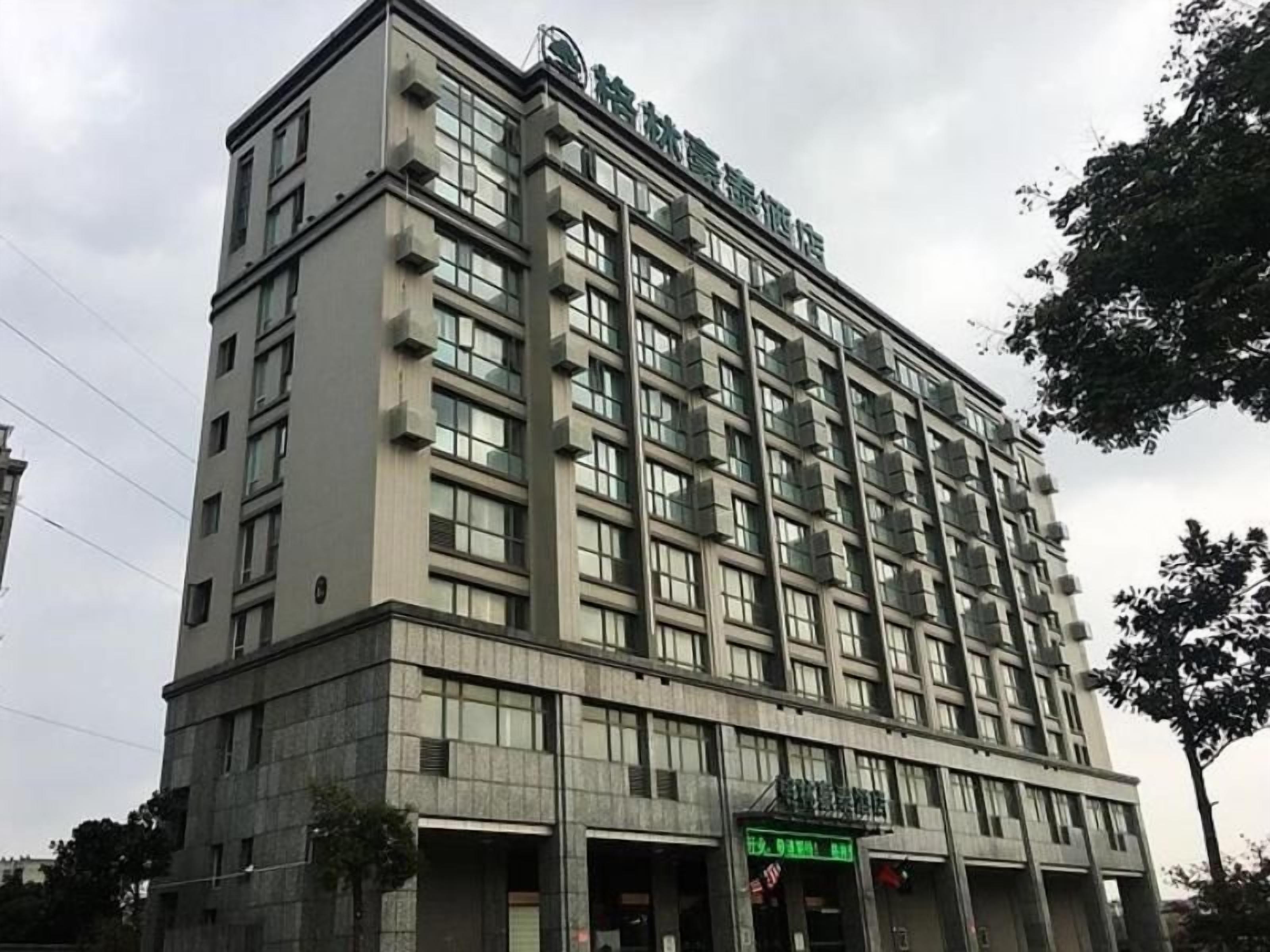 A multi-story hotel with a flat facade, large windows, and a green sign at the entrance.
