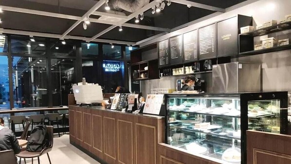 L’intérieur d’un café moderne, avec un comptoir, des panneaux affichant le menu et une vitrine réfrigérée.