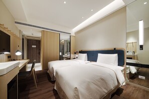 Ein Hotelzimmer mit einem großen Bett, einem Schreibtisch, einem Sessel, einem Spiegel und einer Dusche.