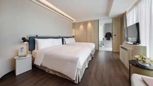 Ein modernes Hotelzimmer mit zwei Betten, einem Fernseher, einem Schreibtisch und einem sichtbaren Badezimmer hinter einer offenen Tür.