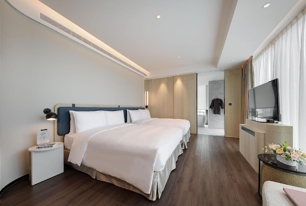 Une chambre d’hôtel moderne, équipée de deux lits, d’une télévision, d’un bureau et d’une salle de bain visible à travers une porte ouverte.