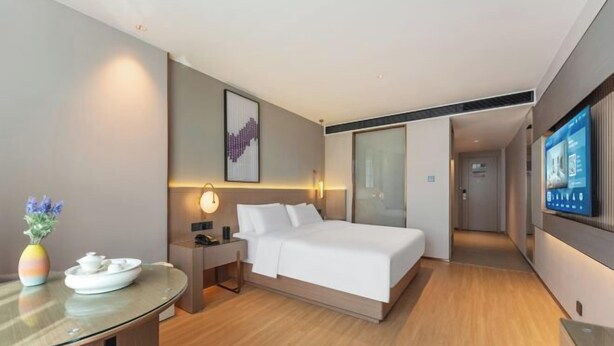 A modern hotel room with a bed, bedside table, lamp, and a TV on the wall. - LAVANDE HOTELS (Chaozhou)