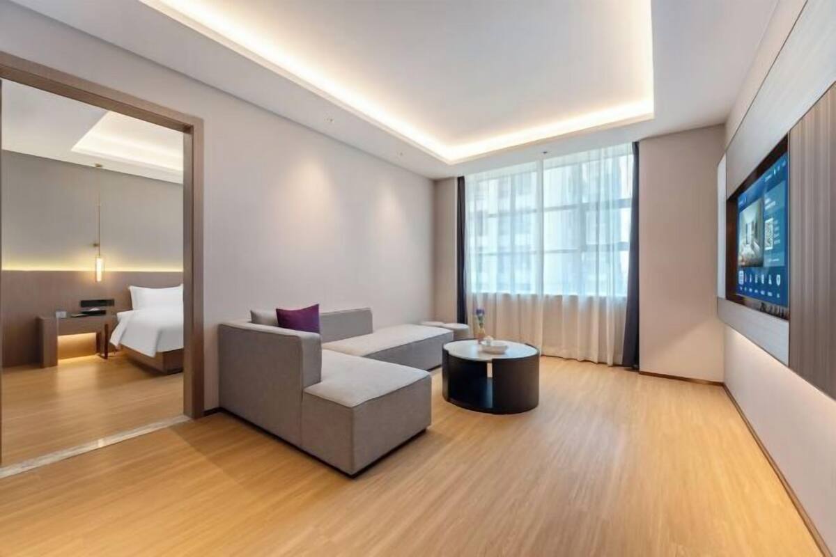 Une chambre d’hôtel moderne équipée d’un canapé, d’une petite table ronde, d’un lit et d’un téléviseur fixé au mur.
