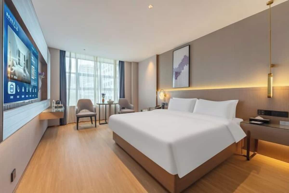 Une chambre d’hôtel moderne équipée d’un grand lit, d’un bureau, d’une chaise et d’un écran de télévision affichant un plan de la chambre.