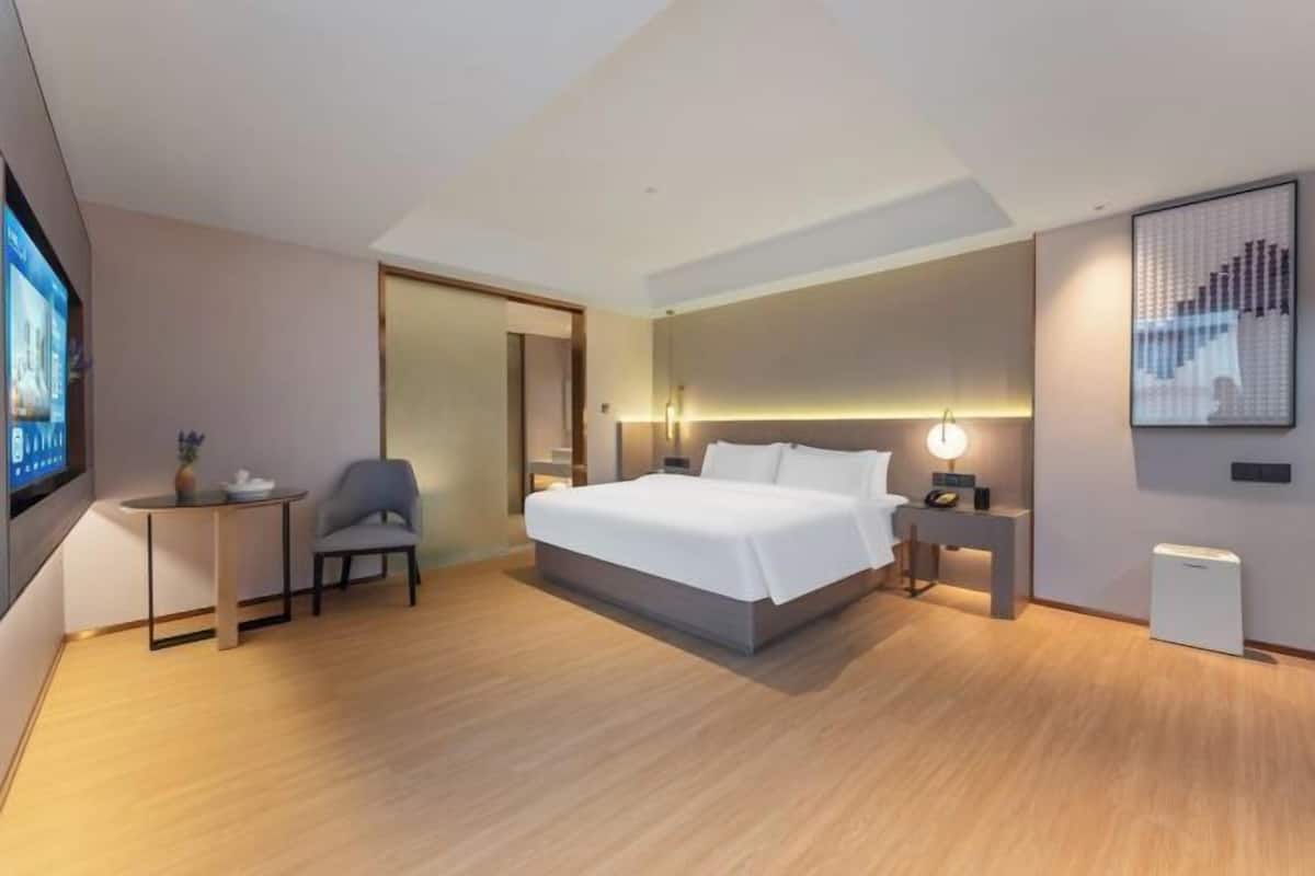 Une chambre d’hôtel moderne équipée d’un lit, d’une table de chevet, d’une chaise, d’un téléviseur et d’une œuvre d’art au mur.