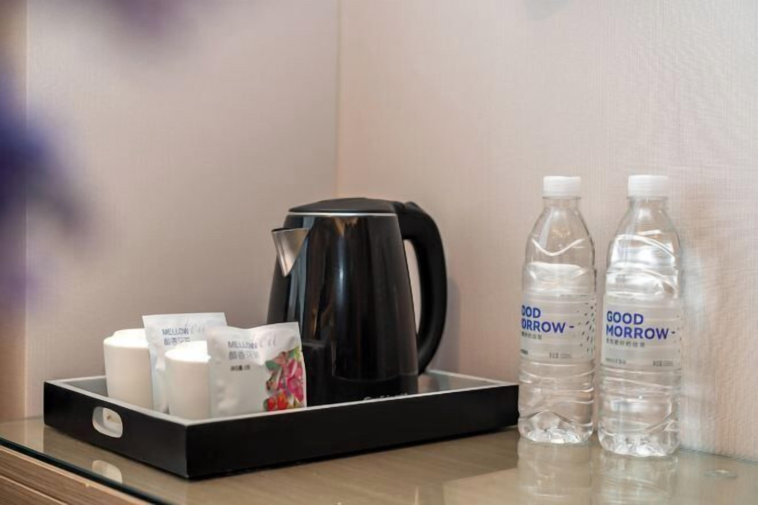 A tray with a black coffee maker, two bottles of water, and several white cups on a glass surface.