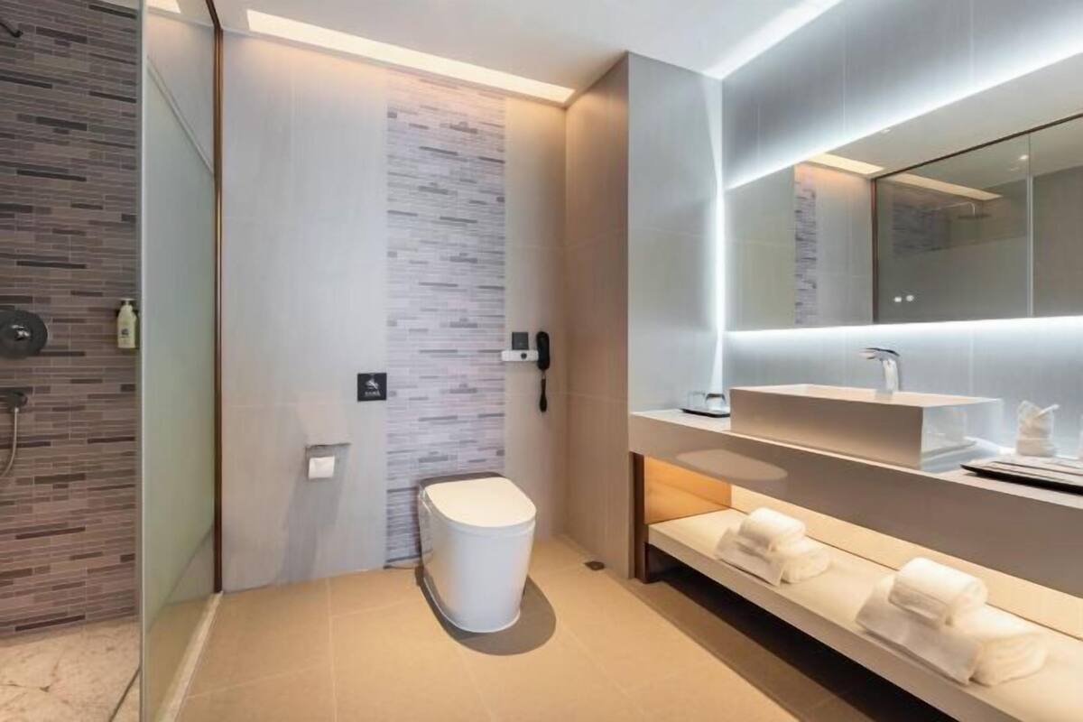 A modern bathroom with a toilet, a shower area, a sink with a mirror, and a towel rack.