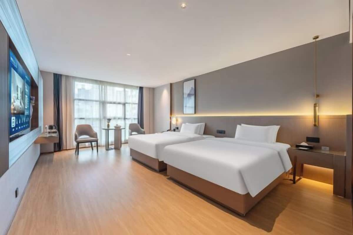 Une chambre d’hôtel avec deux lits, un bureau, une chaise, une télévision et une grande fenêtre.