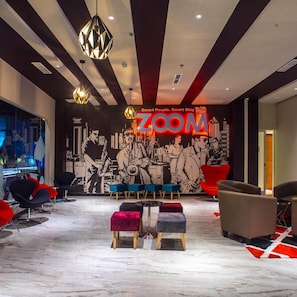 A modern lounge area with a cityscape mural, a 'ZOOM' sign, and contemporary furniture. - Zoom Hotel Mulawarman (Samarinda)