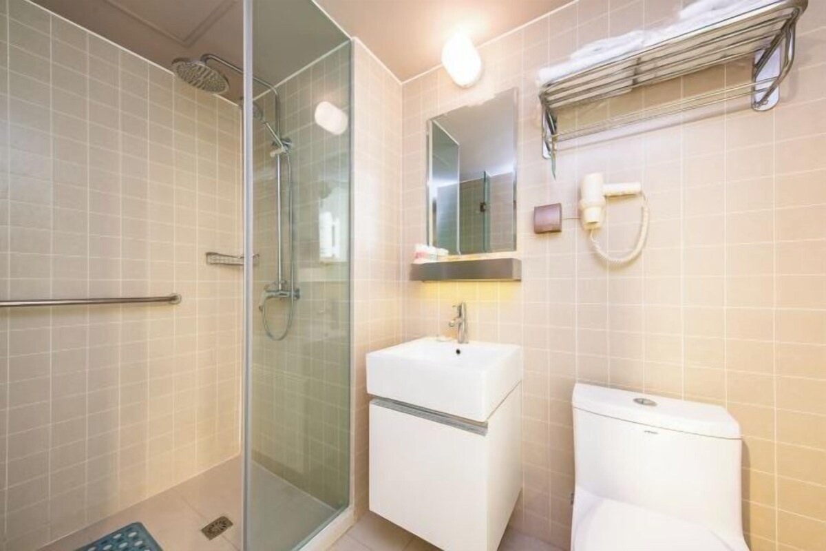 A bathroom with a glass shower enclosure, a white sink, a mirror, and a toilet.