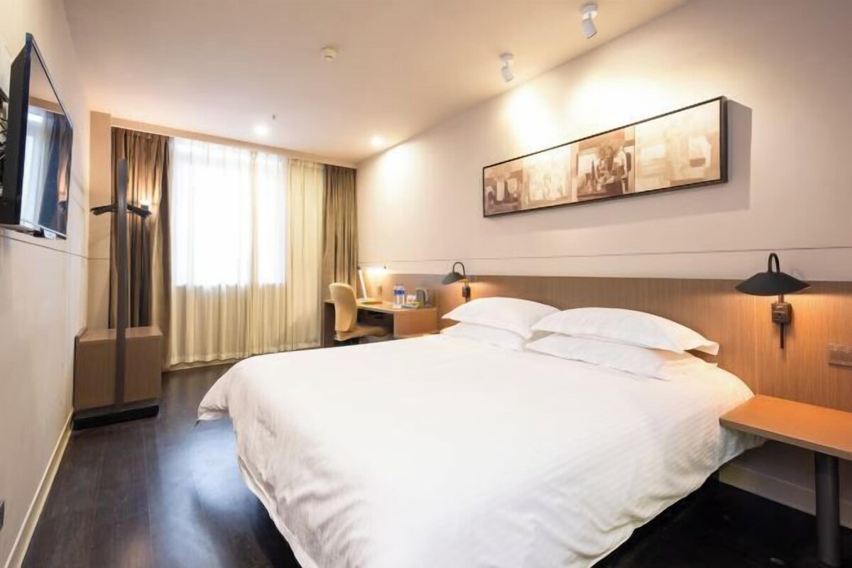A hotel room with a bed, a desk, a chair, a TV, and a window with curtains.