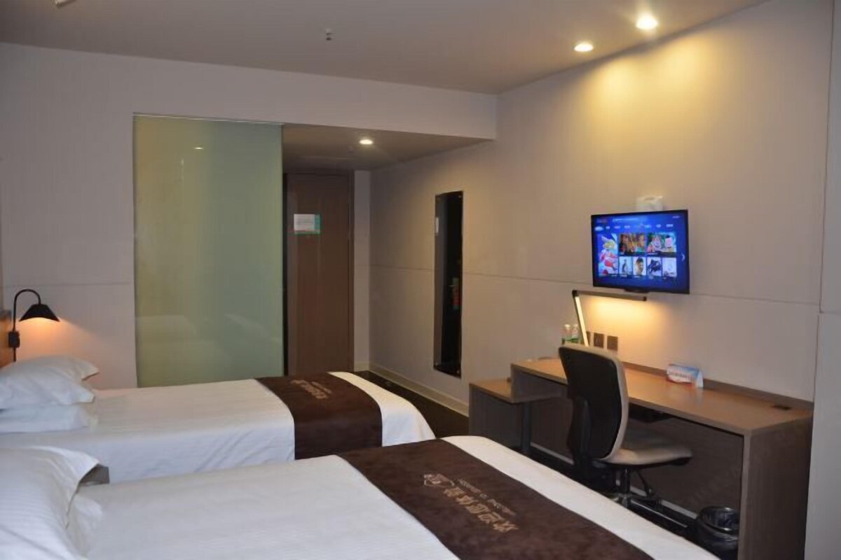 A hotel room with two beds, a desk, a chair, a TV, and a mirror.
