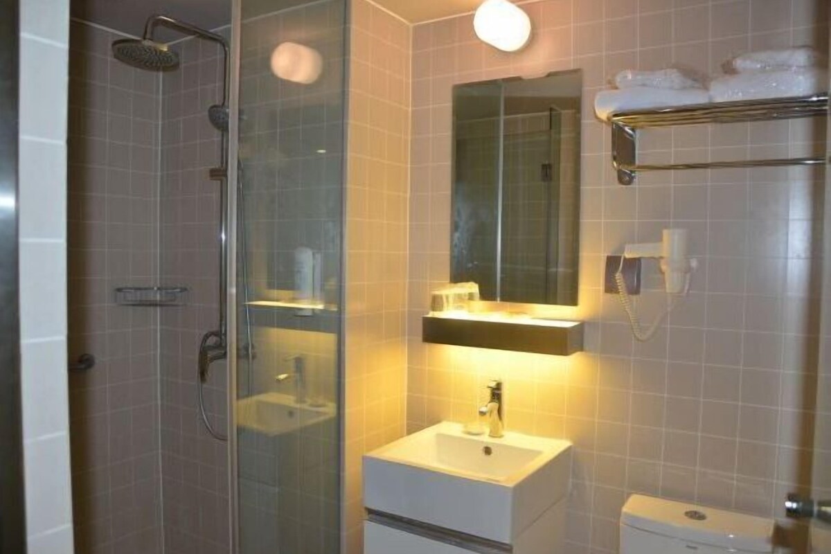 A bathroom with a glass shower enclosure, a white sink, a mirror, and a towel rack.