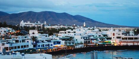 A coastal town with white buildings, a mountain in the background, and a body of water in the foreground.