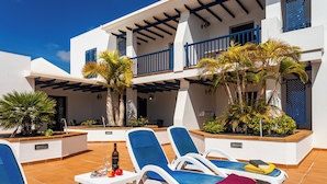 Terraço no telhado com espreguiçadeiras, mesa com garrafa e frutas, e plantas em vasos.
