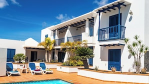 Um edifício de dois andares com piscina, varandas azuis e plantas tropicais.