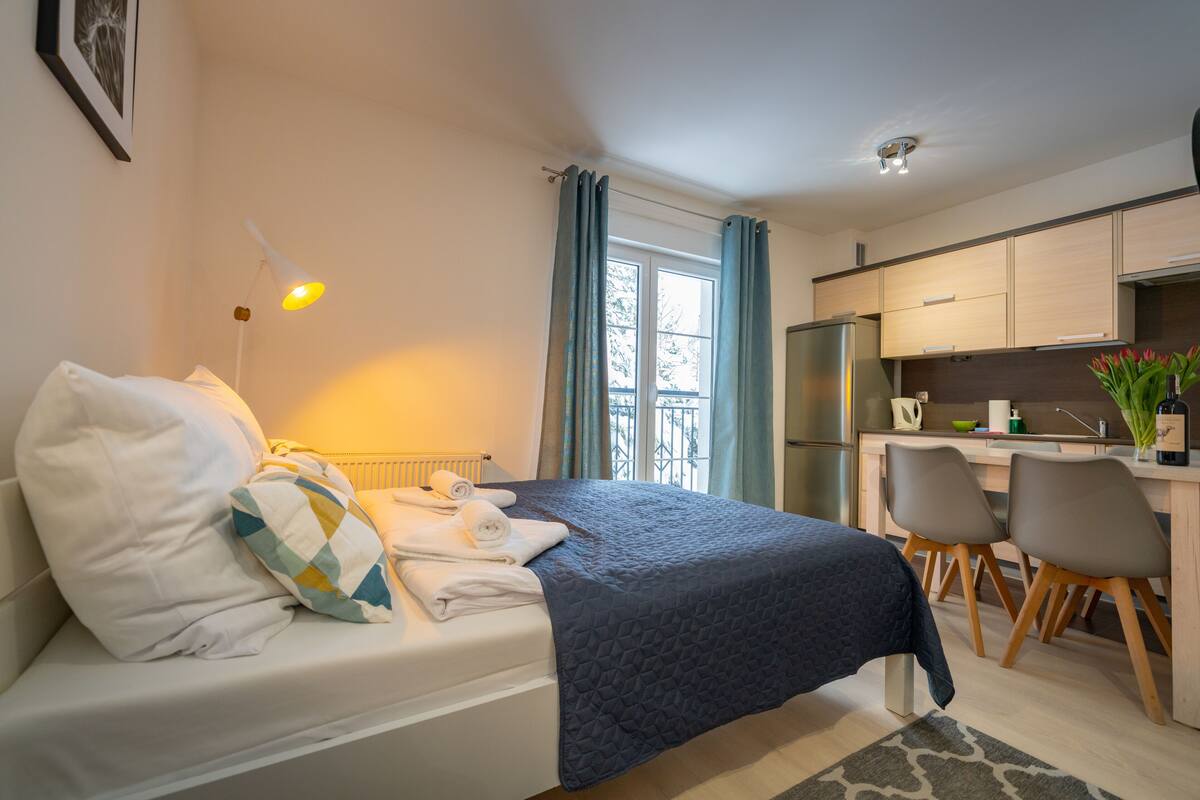 A compact room with a bed, a small desk, and a kitchenette.