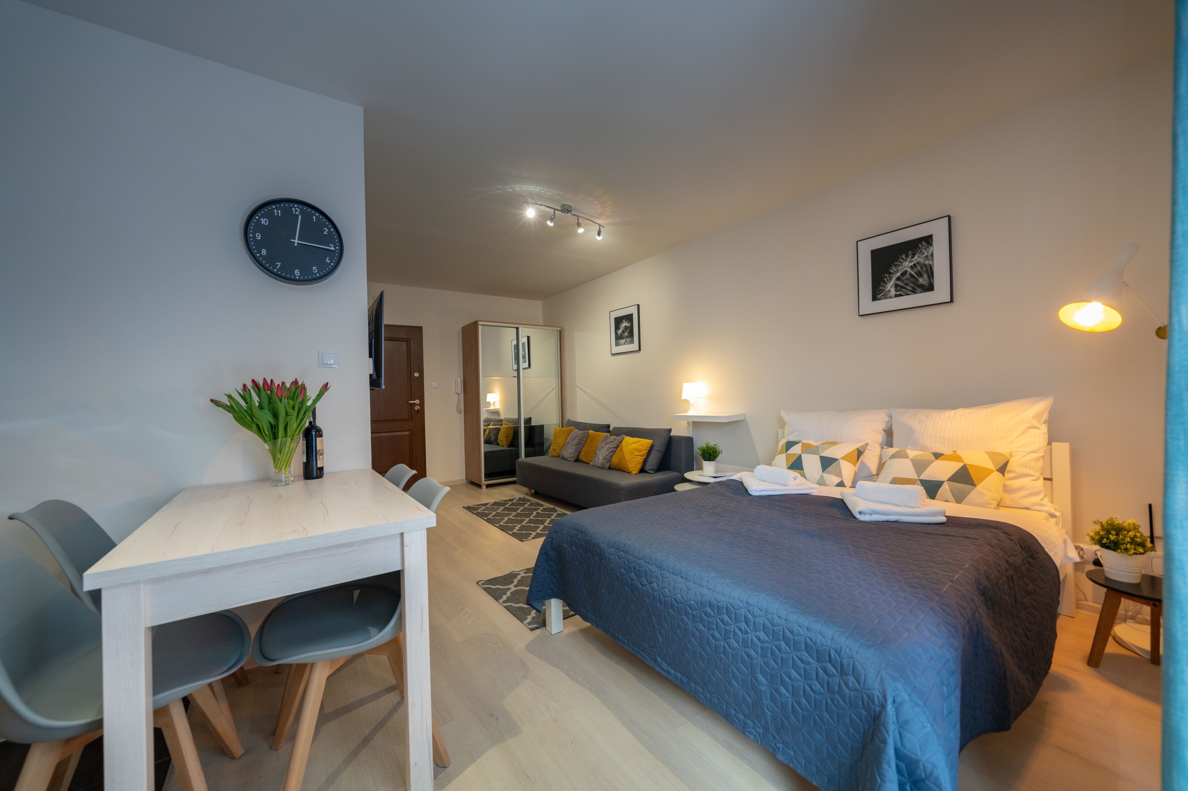 A modern bedroom with a bed, bedside table, lamp, and a clock on the wall.