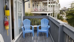 Ein Balkon mit zwei blauen Stühlen, einer gelb-schwarzen Boje und einem weißen Stuhl.