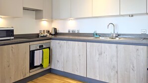 A modern kitchen with wooden cabinets, a built-in oven, a microwave, a kettle, and a sink with a faucet. - Nidus Flat (Cambridge)