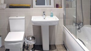 A modern bathroom with a toilet, sink, and glass-enclosed shower. - Nidus Flat (Cambridge)
