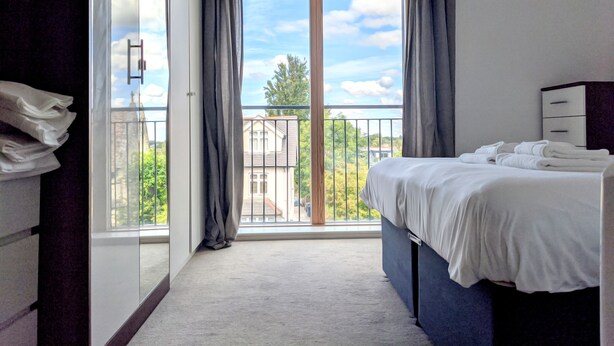 A hotel room with a large window, a bed, a wardrobe, and a balcony with a view of the city. - Nidus Flat (Cambridge)