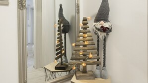 A hallway with a large ornate mirror, a small wooden table with a gnome figure and a Christmas tree, and a geometric metal stand. - Casa Da Ponte (Koper)