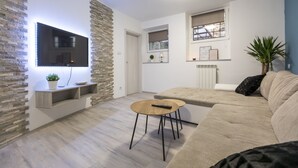 A modern living room with a flat-screen TV mounted on a stone wall, a beige sofa, a wooden coffee table, and a potted plant. - Casa Da Ponte (Koper)