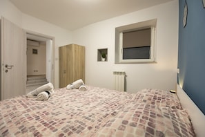 A bedroom with two beds, a wooden wardrobe, a window with a blind, a radiator, and a small plant on the wall. - Casa Da Ponte (Koper)