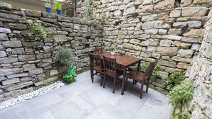A stone wall with a wooden table and chairs in a courtyard. - Casa Da Ponte (Koper)