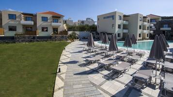 A poolside area with lounge chairs and umbrellas, a stone wall, and modern buildings in the background.