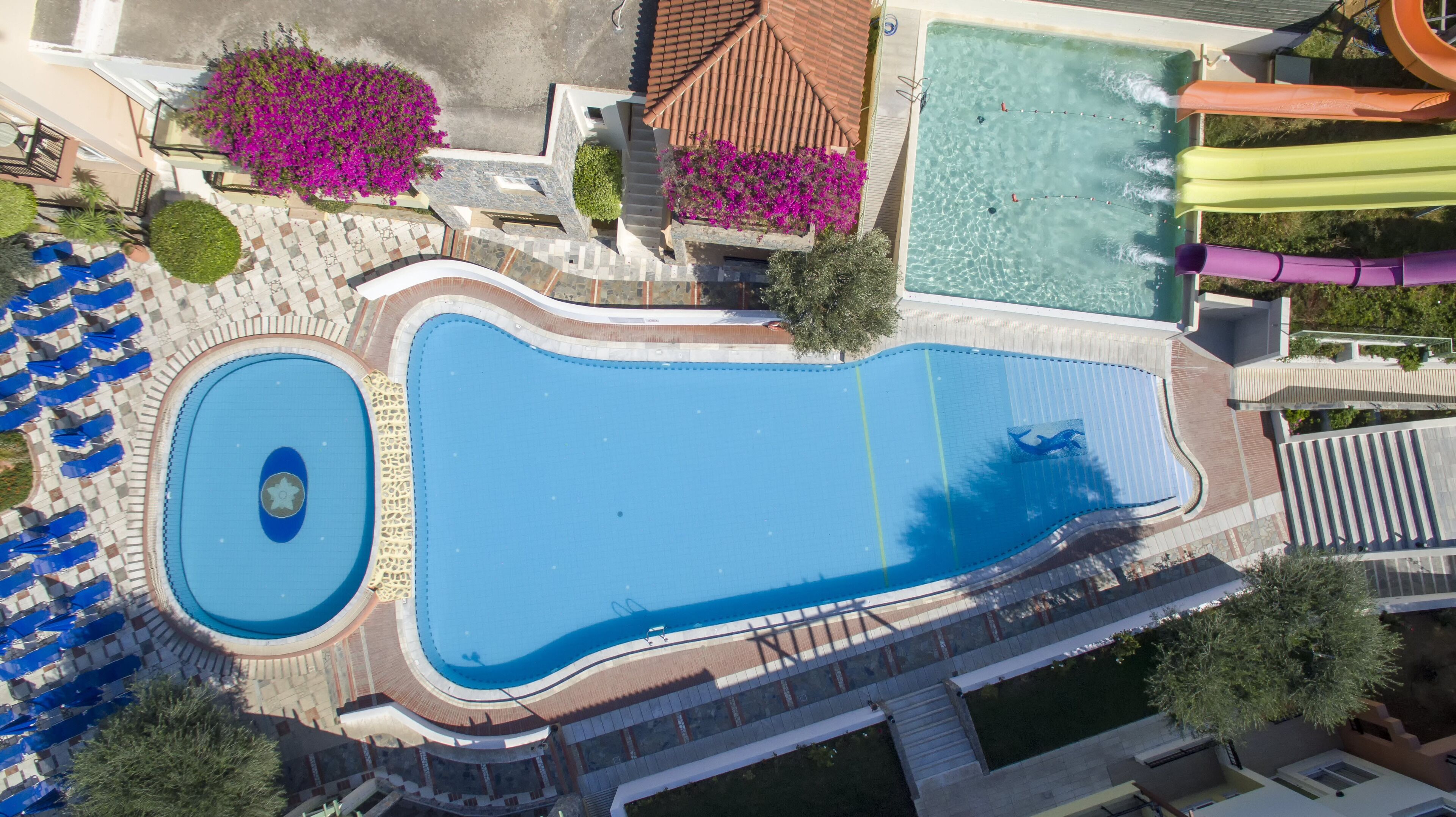 Vista aérea de un complejo de piscinas con varias albercas, un tobogán de agua y zonas de descanso alrededor.