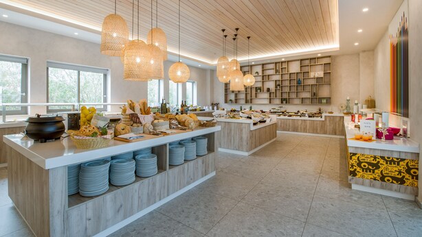 A modern kitchen with wooden countertops, hanging lights, and a variety of food items displayed. - Stefan Village Hotel (Chania)