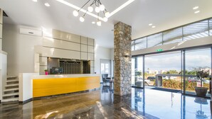 A modern hotel lobby with a reception desk, a stone pillar, and a view of the parking area. - Stefan Village Hotel (Chania)