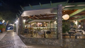 An outdoor dining area with stone flooring, tables, and chairs. - Stefan Village Hotel (Chania)
