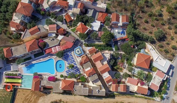 An aerial view of a residential area with multiple houses, a swimming pool, and a small park. - Stefan Village Hotel (Chania)