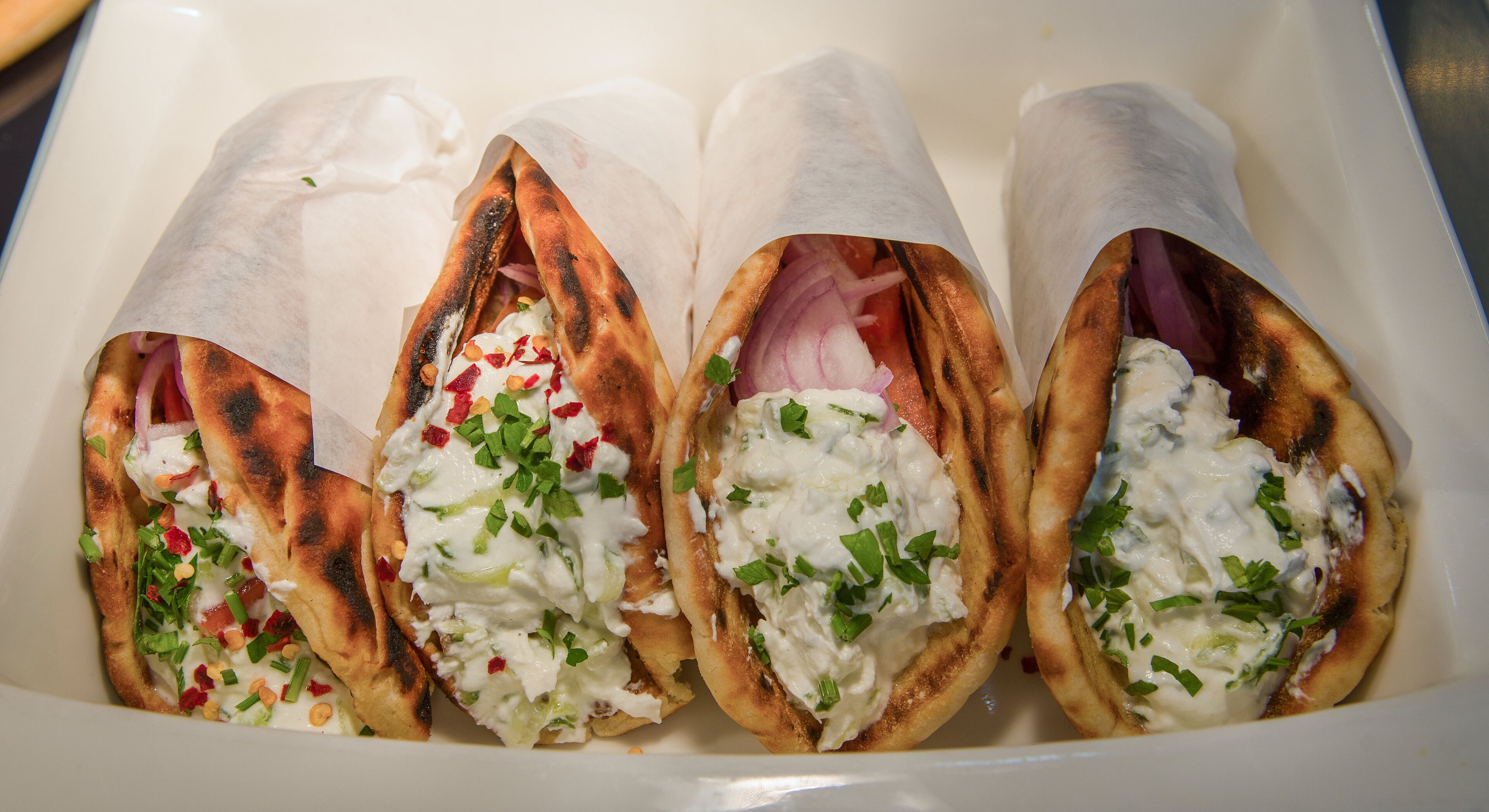 Cuatro wraps con ingredientes, dentro de un recipiente blanco.