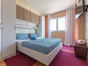 Une chambre à coucher avec un lit, une armoire, une petite table et une fenêtre avec des rideaux.