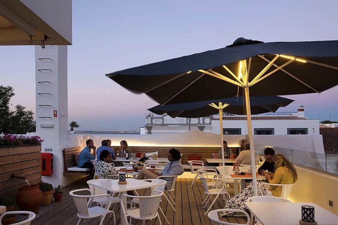 An outdoor dining area with tables and chairs, umbrellas, and a view of a boat in the background.